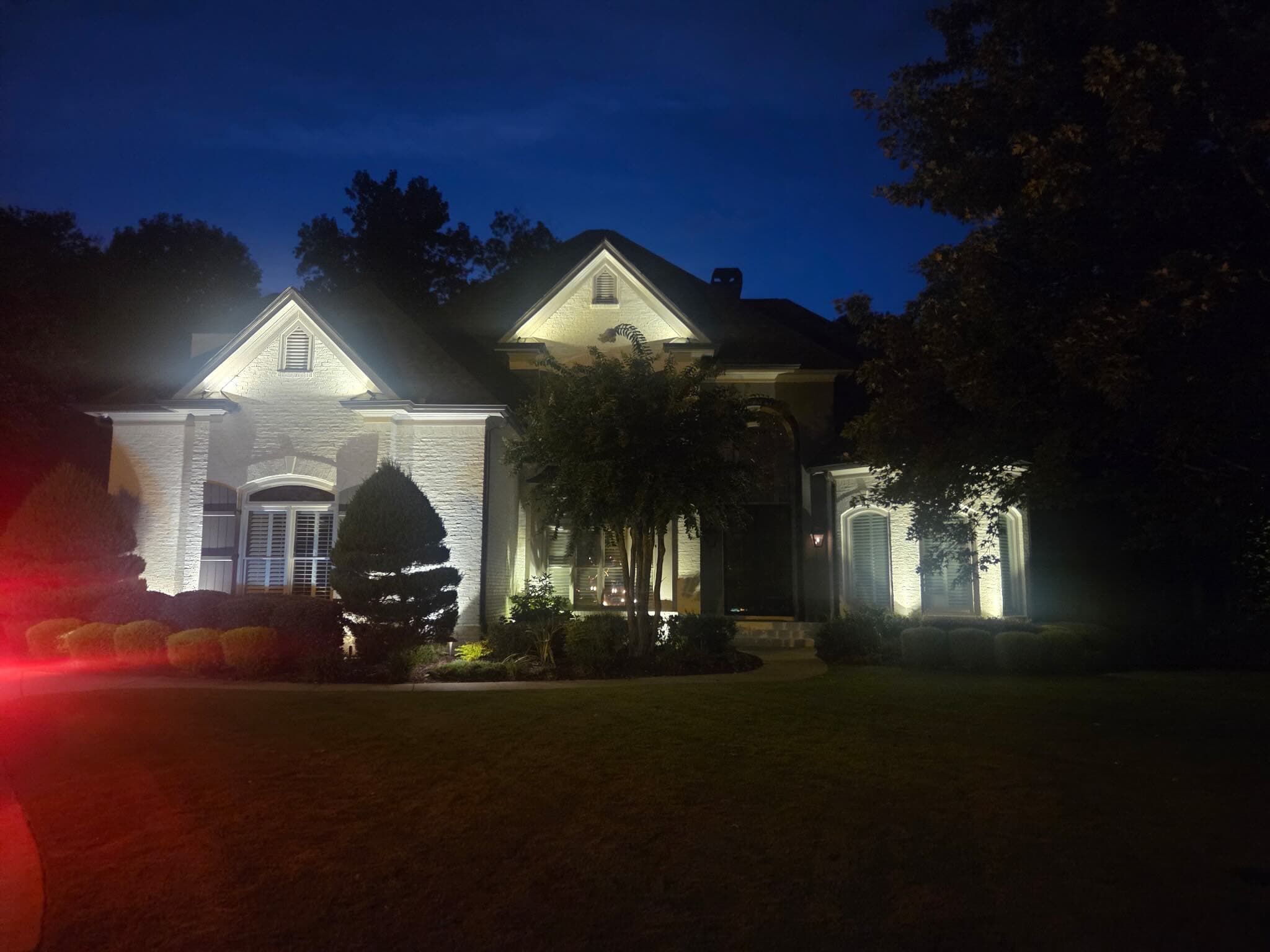 Two-story painted-brick home in Dacula, GA 30019 at blue hour with both front gables uplit in warm white and a crape myrtle accent-lit in the front landscape